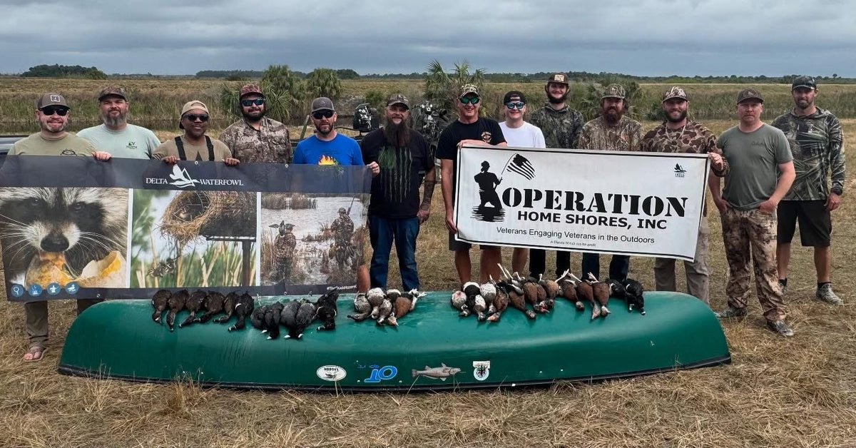 Operation Home Shores volunteers and veterans after a waterfowl hunt, holding the OHS and Delta Waterfowl banners over a canoe